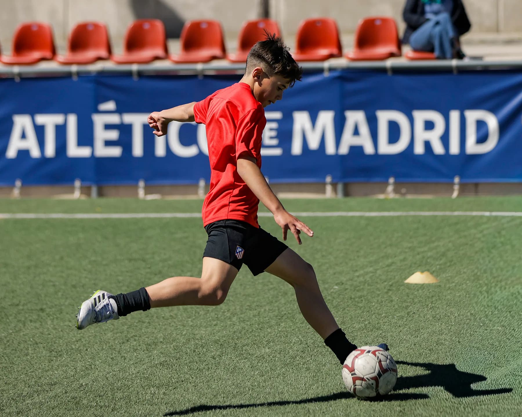 Jugador de la Academia golpea el balón frente a la lona de la Academia Atlético de Madrid